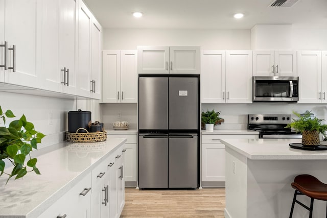 4148 Haleakala Ave, Redding, CA 96001 - kitchen with stainless steel appliances, light countertops, light wood-type flooring, white cabinetry, and a breakfast bar area