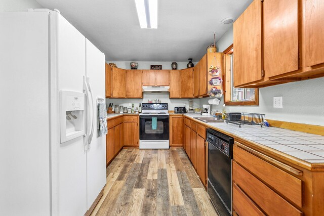 7372 Tahoe Ln, Shingletown, CA 96088 - kitchen with electric range, under cabinet range hood, white refrigerator with ice dispenser, black dishwasher, and light wood-style floors