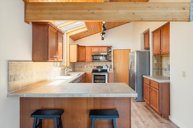 4740 Rainbow, Weed, CA 96094 - kitchen featuring appliances with stainless steel finishes, a peninsula, a skylight, light wood-style flooring, and tile counters