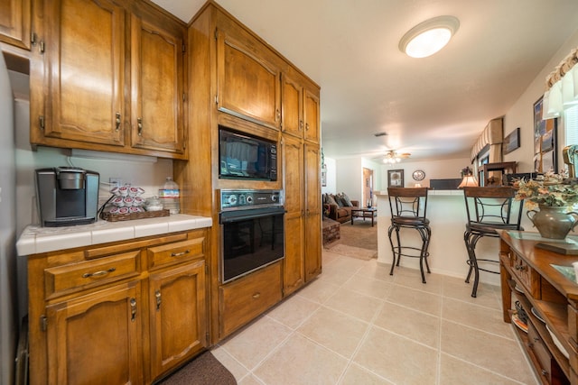 19991 Paso Robles Ave, Redding, CA 96003 - kitchen featuring black appliances, brown cabinets, a kitchen breakfast bar, tile countertops, and a ceiling fan