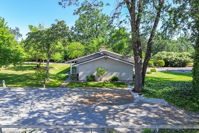 19991 Paso Robles Ave, Redding, CA 96003 - view of side of property featuring stucco siding, a yard, view of wooded area, and a chimney