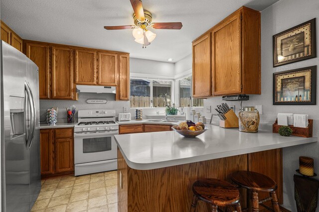 3608 Capricorn Way, Redding, CA 96002 - kitchen featuring white range with gas cooktop, stainless steel refrigerator with ice dispenser, a peninsula, brown cabinetry, and light countertops