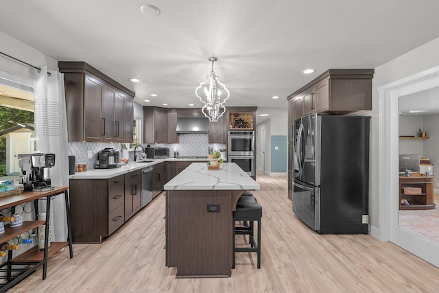 4223 Alta Mesa Dr, Redding, CA 96002 - kitchen with stainless steel appliances, dark brown cabinets, a kitchen island, light wood-style floors, and wall chimney range hood