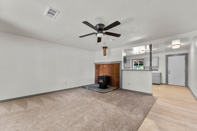 5890 Missouri Ln, Anderson, CA 96007 - unfurnished living room with a wood stove, ceiling fan, baseboards, light wood-style floors, and a textured ceiling