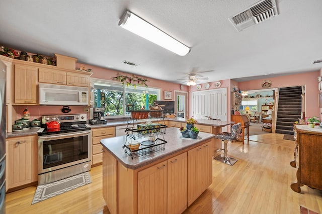 2940 Felstet Ln, Redding, CA 96001 - kitchen with white microwave, electric range, a kitchen island, light wood finished floors, and light brown cabinets