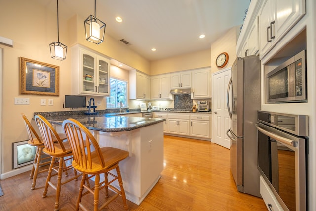 1030 Tulare Ct, Redding, CA 96003 - kitchen featuring appliances with stainless steel finishes, a peninsula, a kitchen breakfast bar, glass insert cabinets, and under cabinet range hood