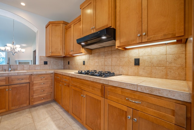 3337 Old Lantern Dr, Redding, CA 96003 - kitchen with under cabinet range hood, a sink, black gas cooktop, a chandelier, and decorative backsplash
