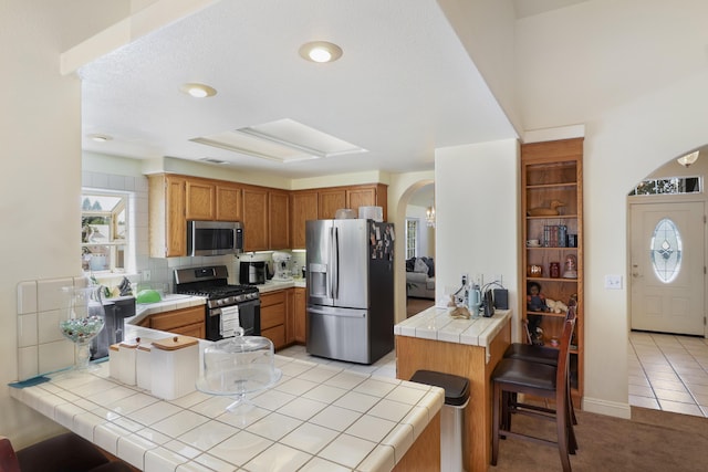 3097 Butterfly Ln, Shasta Lake, CA 96019 - kitchen featuring stainless steel appliances, arched walkways, a peninsula, tile countertops, and a kitchen bar