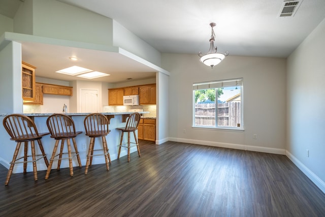 3255 Wandsworth Dr, Shasta Lake, CA 96019 - kitchen featuring white microwave, a peninsula, dark wood-style flooring, a kitchen breakfast bar, and brown cabinets