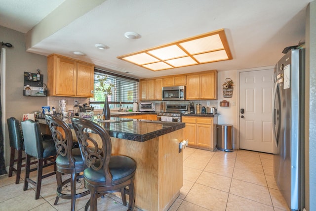 1136 Woodland Ter, Redding, CA 96002 - kitchen with stainless steel appliances, a peninsula, a breakfast bar area, dark countertops, and light tile patterned floors