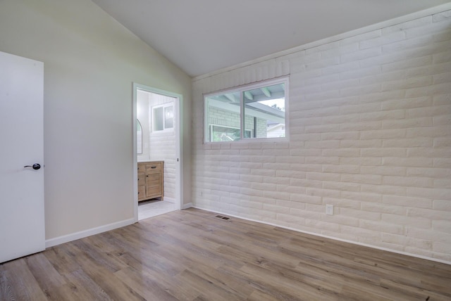 3090 Inez St, Redding, CA 96002 - empty room featuring wood finished floors, vaulted ceiling, baseboards, and brick wall