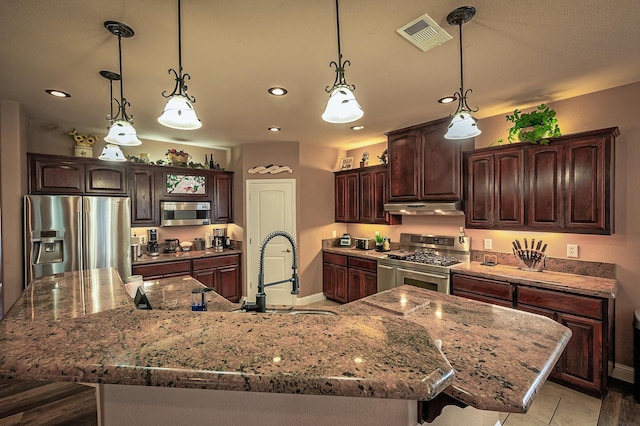13787 Walter Ave, Redding, CA 96003 - kitchen with appliances with stainless steel finishes, under cabinet range hood, dark brown cabinets, a large island with sink, and a sink