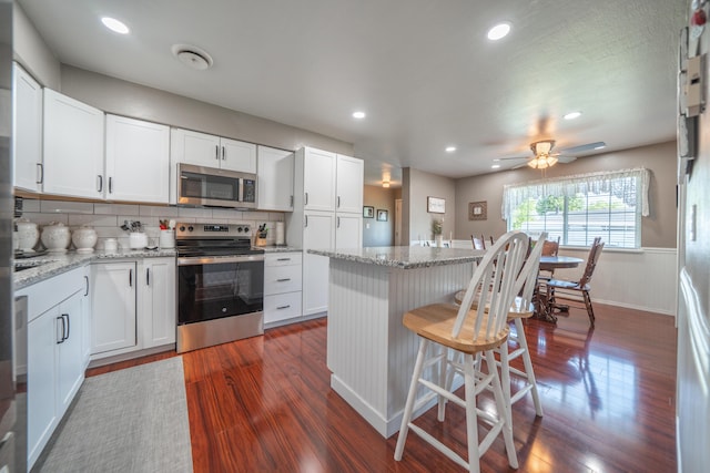 37255 Carson St, Burney, CA 96013 - kitchen with appliances with stainless steel finishes, dark wood-style flooring, a kitchen bar, white cabinetry, and wainscoting