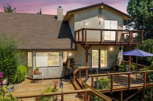 2173 Oak Ridge Dr, Redding, CA 96001 - back of house at dusk with a balcony, a chimney, stucco siding, a wooden deck, and a shingled roof