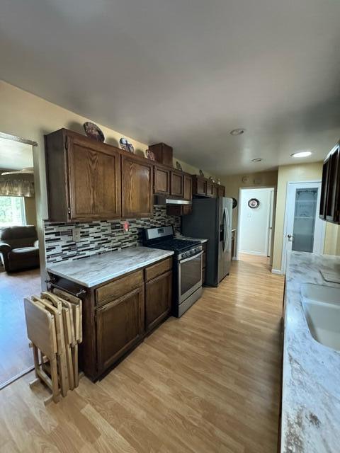 37023 Park Ave, Burney, CA 96013 - kitchen with stainless steel appliances, light countertops, light wood-style floors, backsplash, and dark brown cabinets