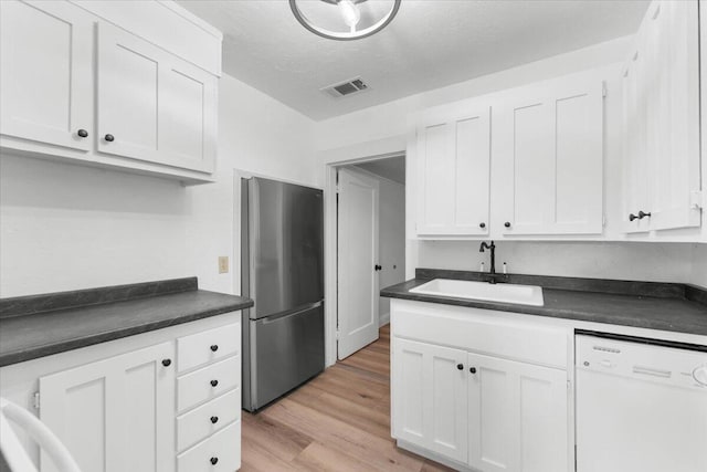 830 W St, Redding, CA 96001 - kitchen with freestanding refrigerator, white dishwasher, dark countertops, white cabinetry, and a textured ceiling