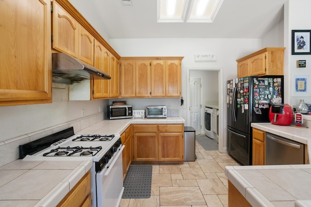 2834 Aspen Glow Ln, Redding, CA 96001 - kitchen with stainless steel appliances, washer / dryer, tile counters, under cabinet range hood, and light stone finish flooring