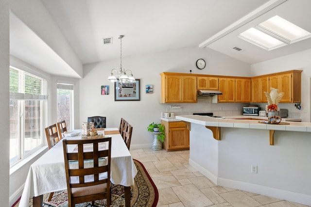 2834 Aspen Glow Ln, Redding, CA 96001 - kitchen featuring tile counters, a breakfast bar area, light stone finish flooring, pendant lighting, and under cabinet range hood