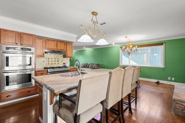 3428 Adams Ln, Redding, CA 96002 - kitchen featuring stainless steel double oven, ornamental molding, under cabinet range hood, backsplash, and a kitchen bar