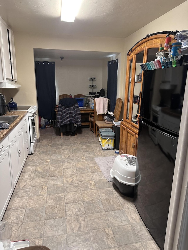 1310 Olive St, Redding, CA 96001 - kitchen with white electric range, white cabinets, freestanding refrigerator, extractor fan, and stone finish floors