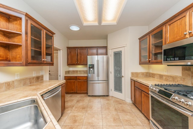 2926 Chaucer Way, Shasta Lake, CA 96019 - kitchen with stainless steel appliances, light tile patterned floors, glass insert cabinets, tile countertops, and brown cabinetry