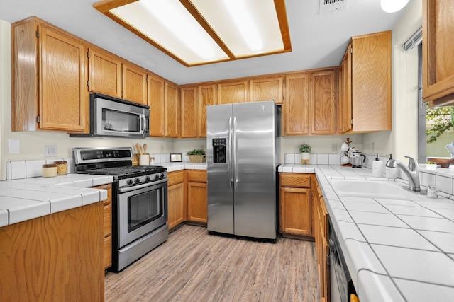2820 Howard Dr, Redding, CA 96001 - kitchen featuring appliances with stainless steel finishes, tile counters, light wood-style floors, and brown cabinets