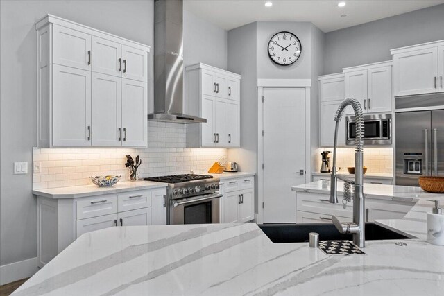 19580 Mockingbird Ln, Redding, CA 96002 - kitchen featuring wall chimney range hood, built in appliances, tasteful backsplash, white cabinets, and light stone counters