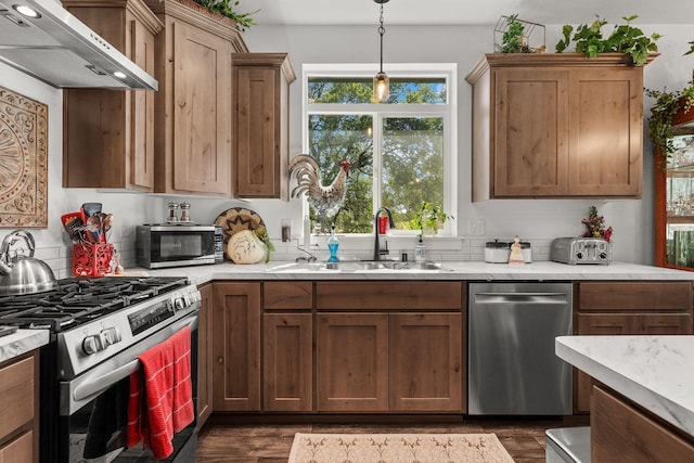 18710 Saddleback Ridge Rd, Cottonwood, CA 96022 - kitchen featuring appliances with stainless steel finishes, under cabinet range hood, dark wood-style flooring, hanging light fixtures, and brown cabinetry