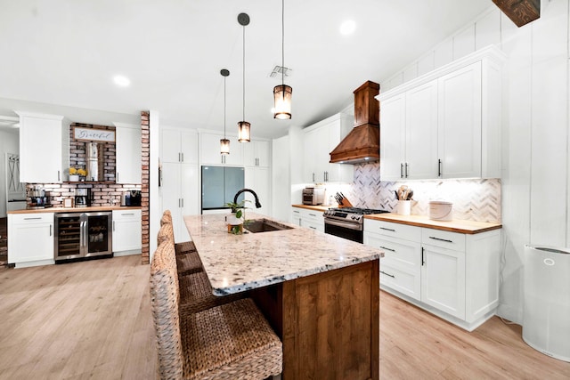 3075 Forest Hills Dr, Redding, CA 96002 - kitchen featuring wine cooler, stainless steel range oven, premium range hood, decorative backsplash, and light wood-style flooring