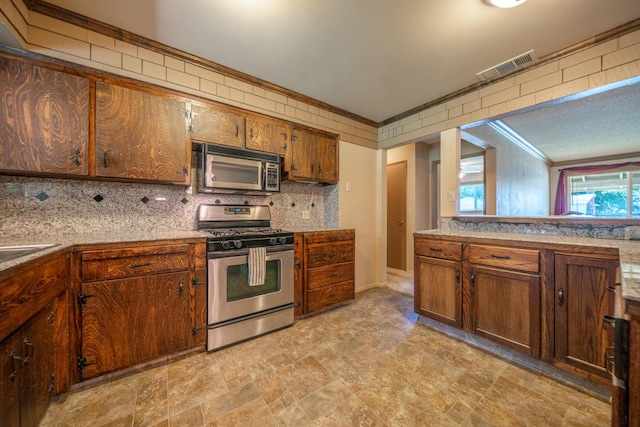 2076 Merle Dr, Redding, CA 96001 - kitchen featuring appliances with stainless steel finishes, ornamental molding, stone finish flooring, backsplash, and light countertops