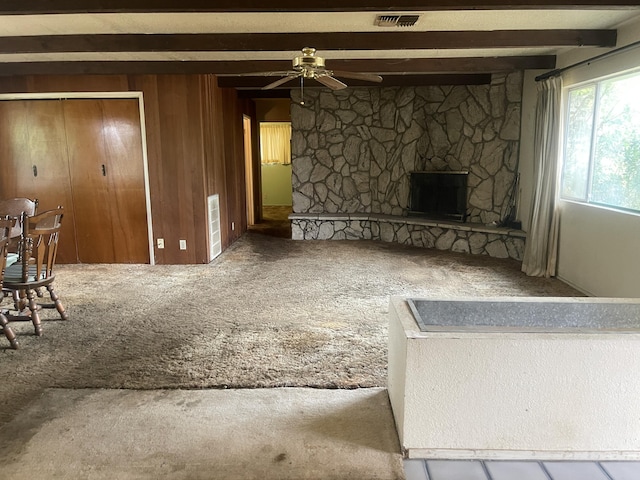 1110 Dusty Ln, Redding, CA 96002 - unfurnished living room featuring carpet flooring, beam ceiling, a ceiling fan, a stone fireplace, and wooden walls