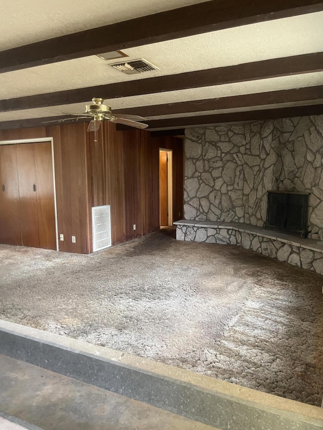 1110 Dusty Ln, Redding, CA 96002 - unfurnished living room featuring beam ceiling, ceiling fan, carpet flooring, wooden walls, and a stone fireplace