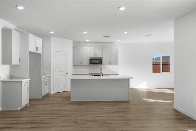 876 Wind Cove Dr, Redding, CA 96001 - kitchen featuring stainless steel microwave, light wood-style flooring, recessed lighting, a kitchen island with sink, and light countertops