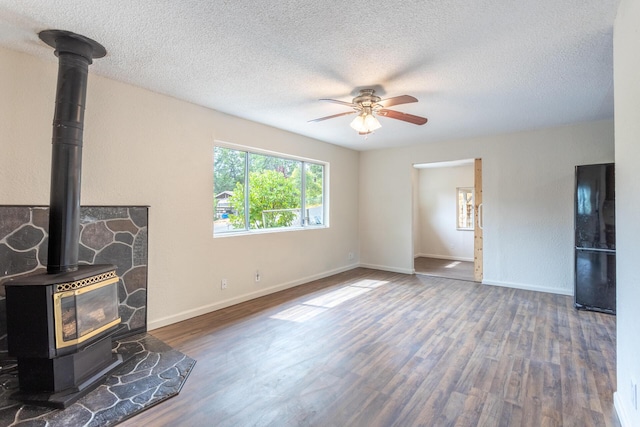1535 Provo Ave, Shasta Lake, CA 96019 - unfurnished living room featuring a wood stove, wood finished floors, a textured ceiling, and a ceiling fan