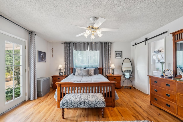 14480 Warren Ave, Red Bluff, CA 96080 - bedroom with light wood-type flooring, a barn door, access to outside, a textured ceiling, and ceiling fan