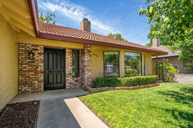3628 Somerset Ave, Redding, CA 96002 - entrance to property featuring a chimney, a tile roof, stucco siding, a lawn, and brick siding