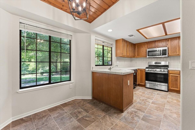3628 Somerset Ave, Redding, CA 96002 - kitchen featuring stainless steel appliances, tile counters, brown cabinets, tasteful backsplash, and light stone finish flooring