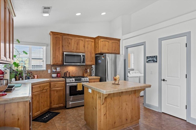 2236 Lonigan Ct, Redding, CA 96001 - kitchen featuring stainless steel appliances, washer and dryer, vaulted ceiling, a kitchen island, and tasteful backsplash