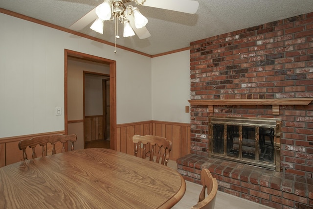 30839 Tinkerbell Ln, Shingletown, CA 96088 - dining space with ceiling fan, a textured ceiling, a wainscoted wall, ornamental molding, and a brick fireplace