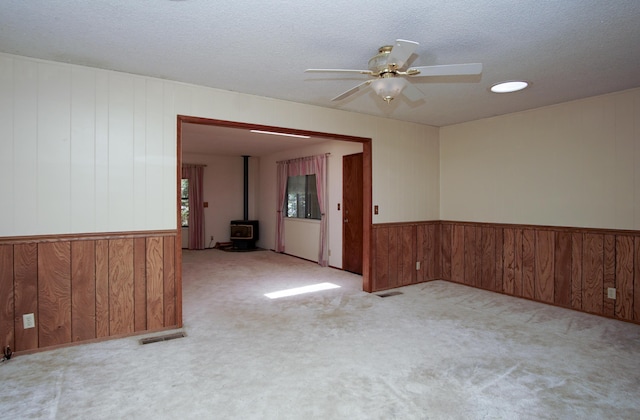 30839 Tinkerbell Ln, Shingletown, CA 96088 - spare room featuring a wood stove, ceiling fan, wooden walls, carpet flooring, and a textured ceiling