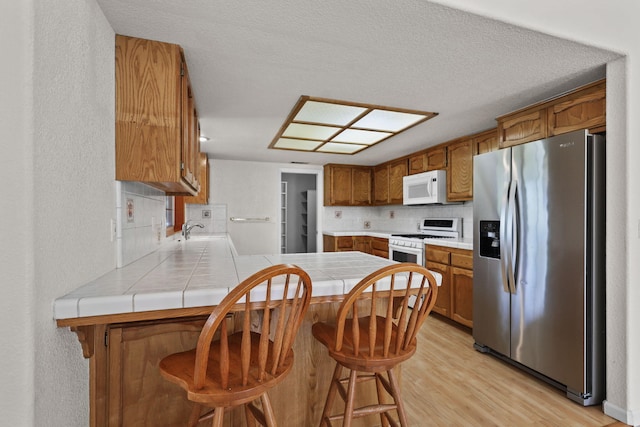 12526 Glide Way, Redding, CA 96003 - kitchen with white appliances, a peninsula, tile countertops, brown cabinetry, and tasteful backsplash