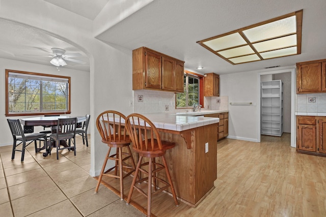 12526 Glide Way, Redding, CA 96003 - kitchen featuring tile counters, tasteful backsplash, brown cabinetry, a breakfast bar area, and a peninsula