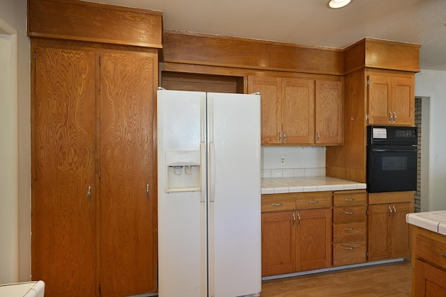 210 Sherman St, Yreka, CA 96097 - kitchen featuring white fridge with ice dispenser, black oven, light wood finished floors, and brown cabinets