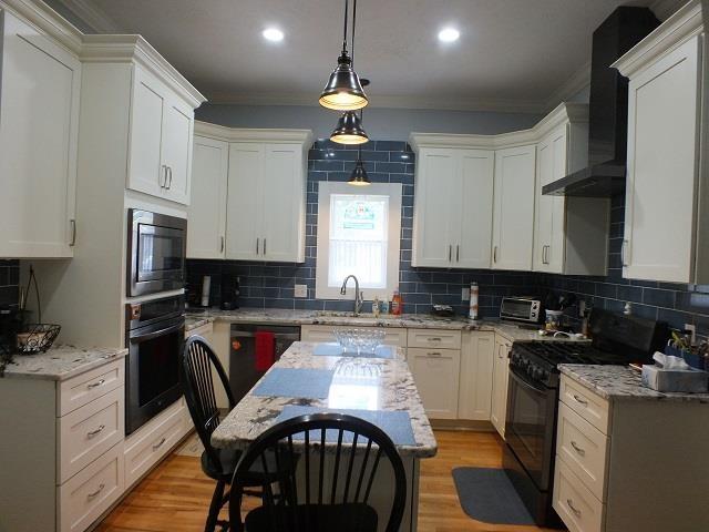 kitchen with light stone countertops, backsplash, black appliances, and wall chimney range hood