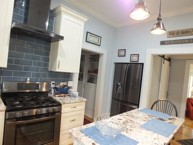 kitchen with black refrigerator with ice dispenser, stainless steel range with gas stovetop, light stone countertops, wall chimney exhaust hood, and backsplash