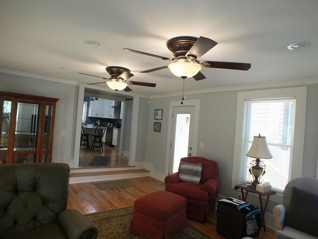 living room featuring ceiling fan, ornamental molding, and wood-type flooring