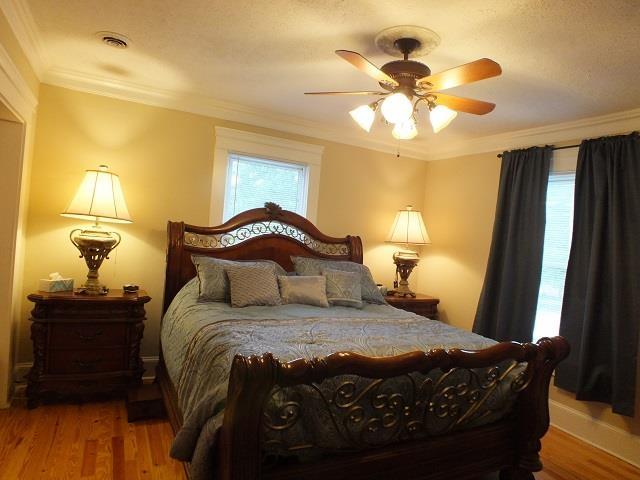 bedroom with ceiling fan, ornamental molding, and wood-type flooring