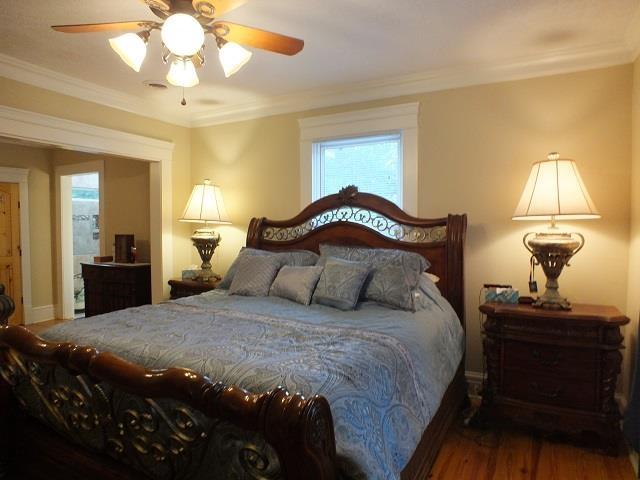 bedroom with ceiling fan, crown molding, and dark wood-type flooring