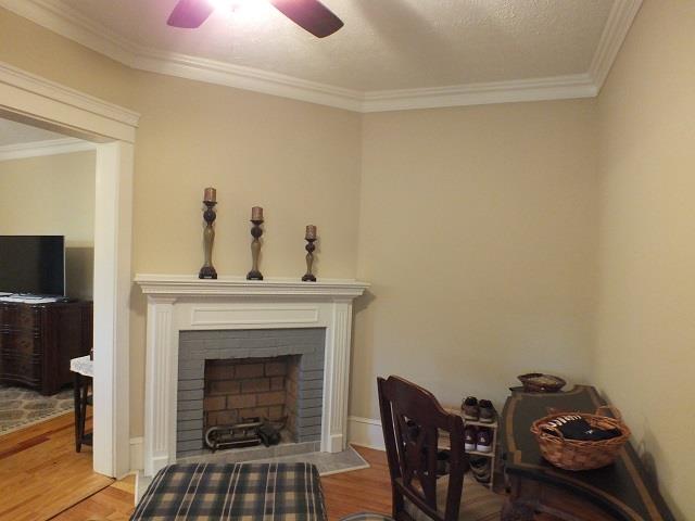 home office with a fireplace, crown molding, ceiling fan, and light wood-type flooring