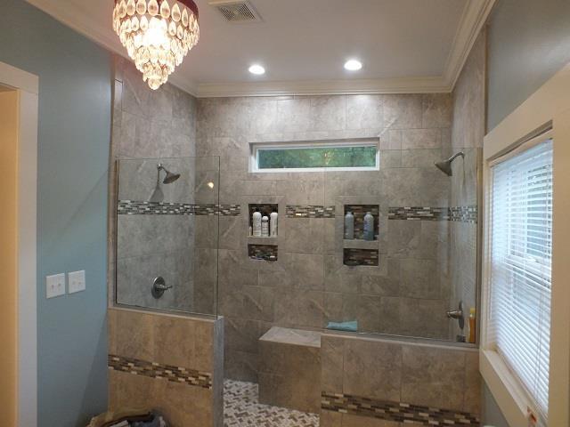 bathroom with a tile shower, a wealth of natural light, and ornamental molding